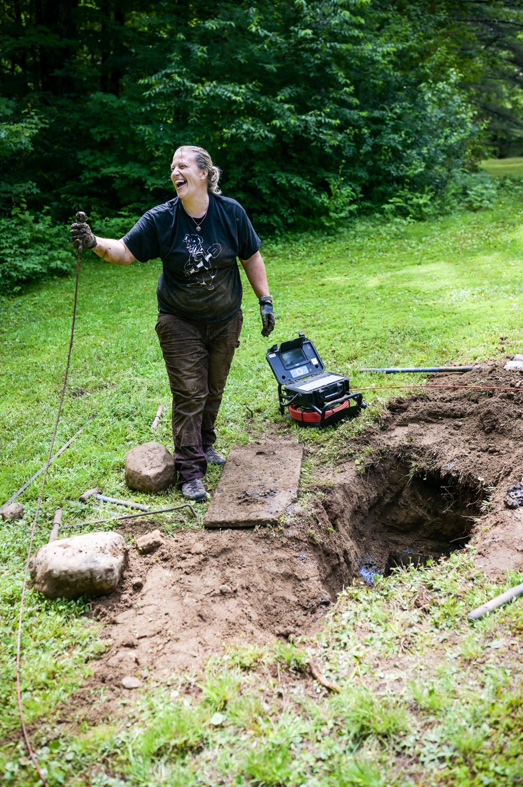 A Turner Septic technician laughing while running camera equipment at an open septic tank.