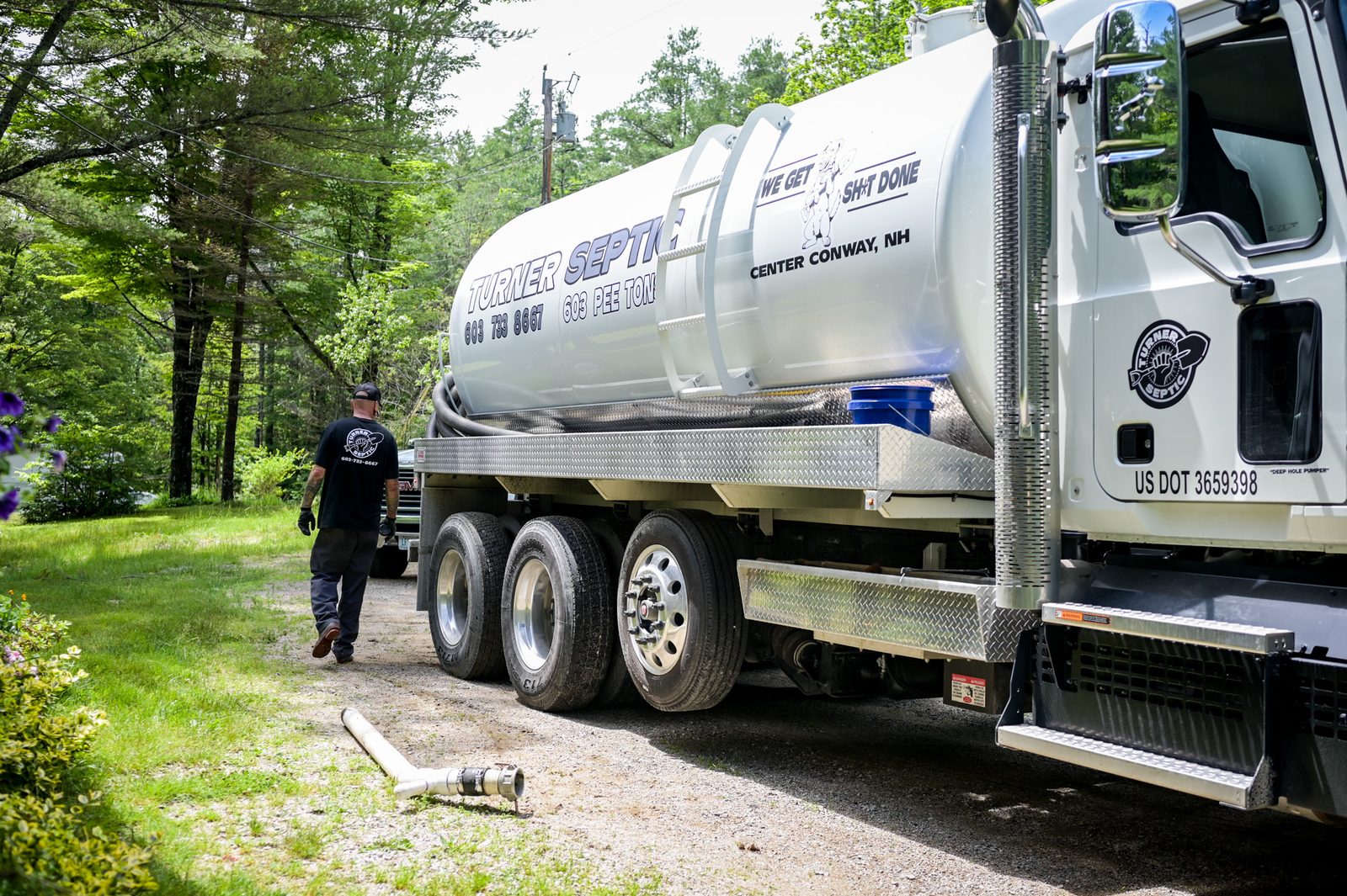 A Turner Septic pump truck parked at a home on a wooded driveway, with a technician walking beside it.