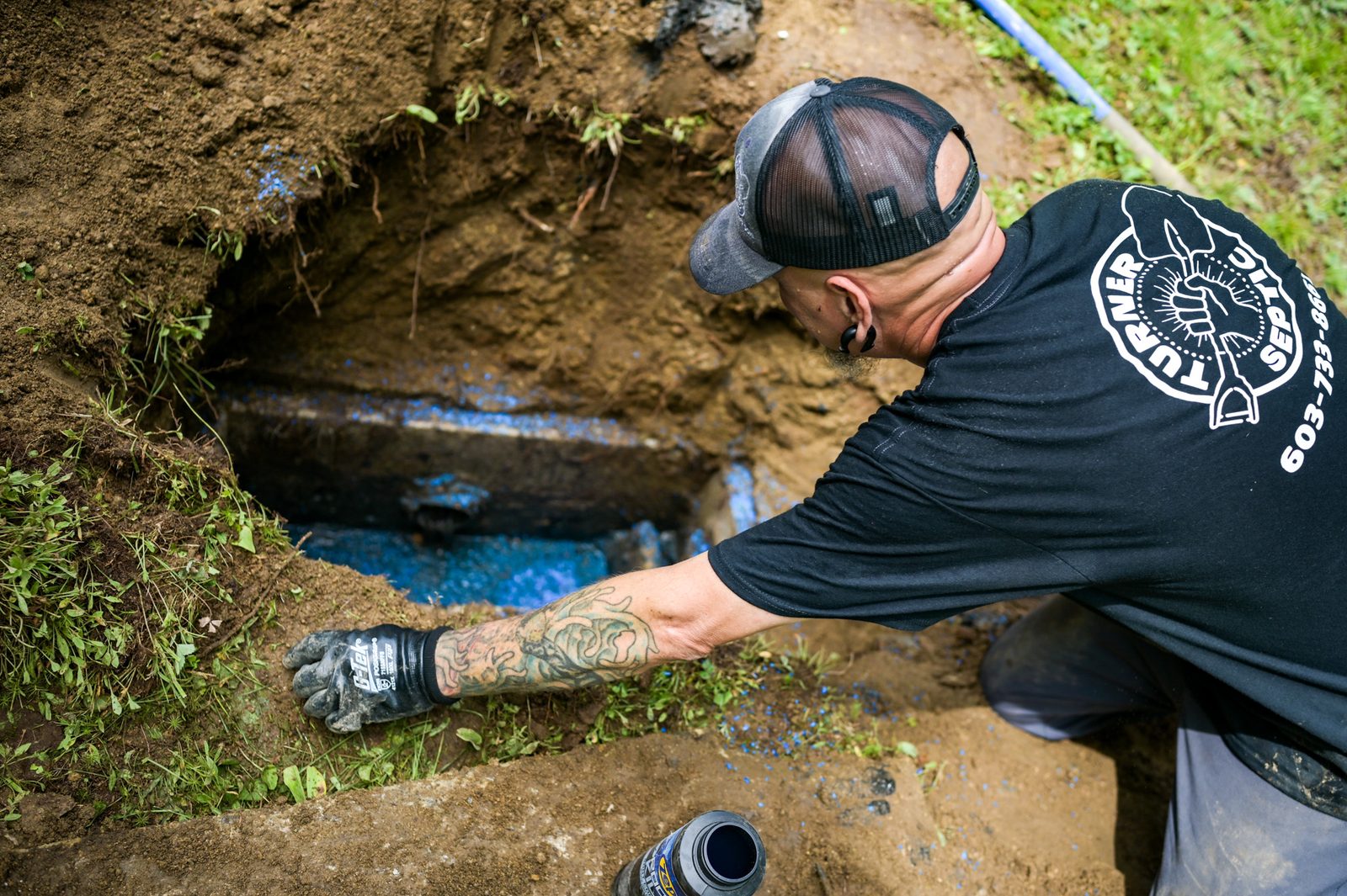 A Turner Septic technician working at an uncovered septic tank in an excavated hole.